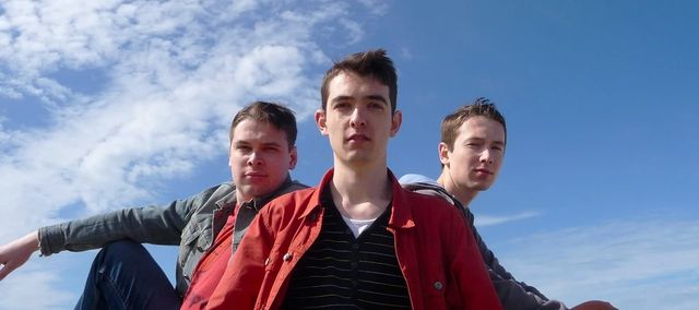 All three band members against a blue sky
